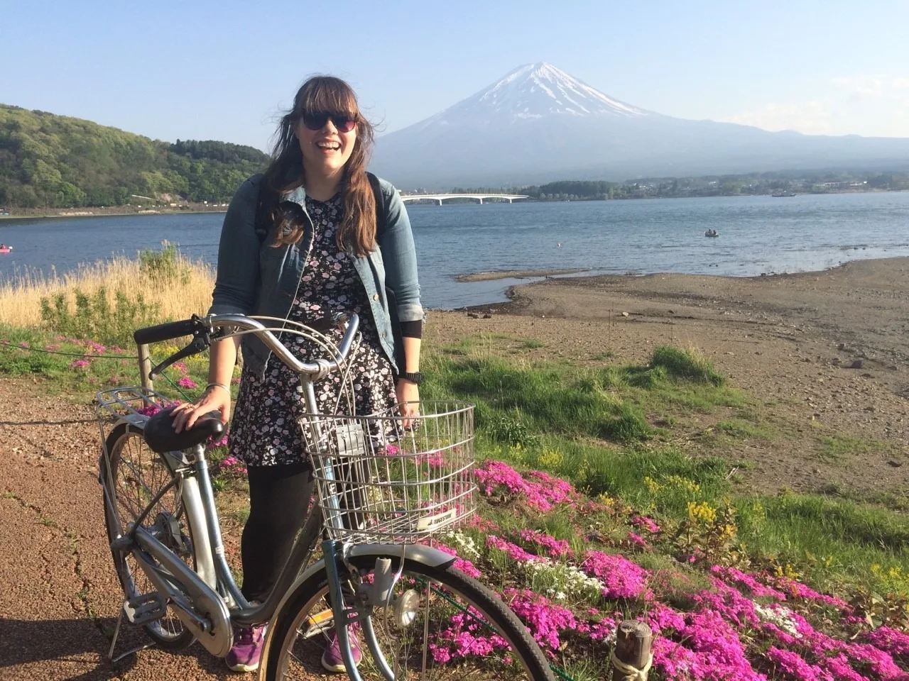 lauren standing with a bicycle, with mount fuji in the distance behind her, and kawaguchiko five lakes. in japan