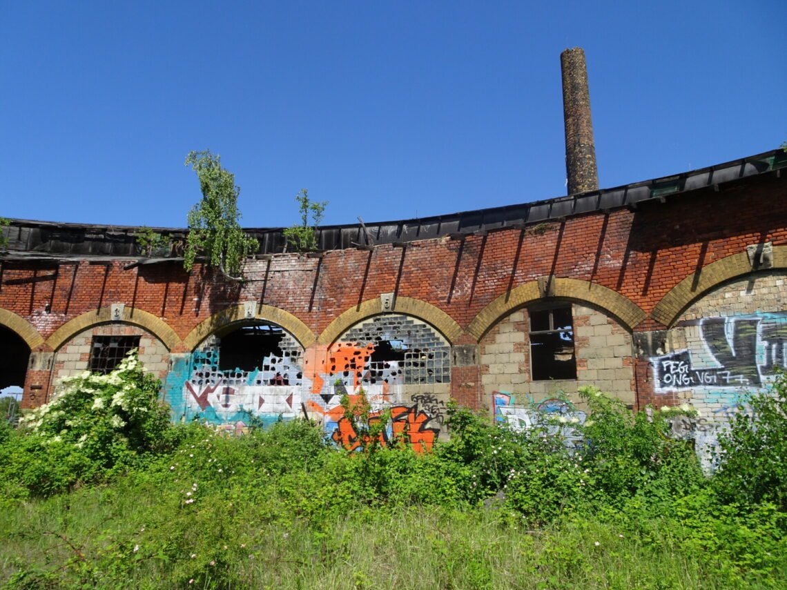 graffiti and broken windows on old red brick archway building and tree overgrowth