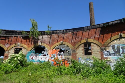 graffiti and broken windows on old red brick archway building and tree overgrowth