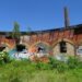 graffiti and broken windows on old red brick archway building and tree overgrowth