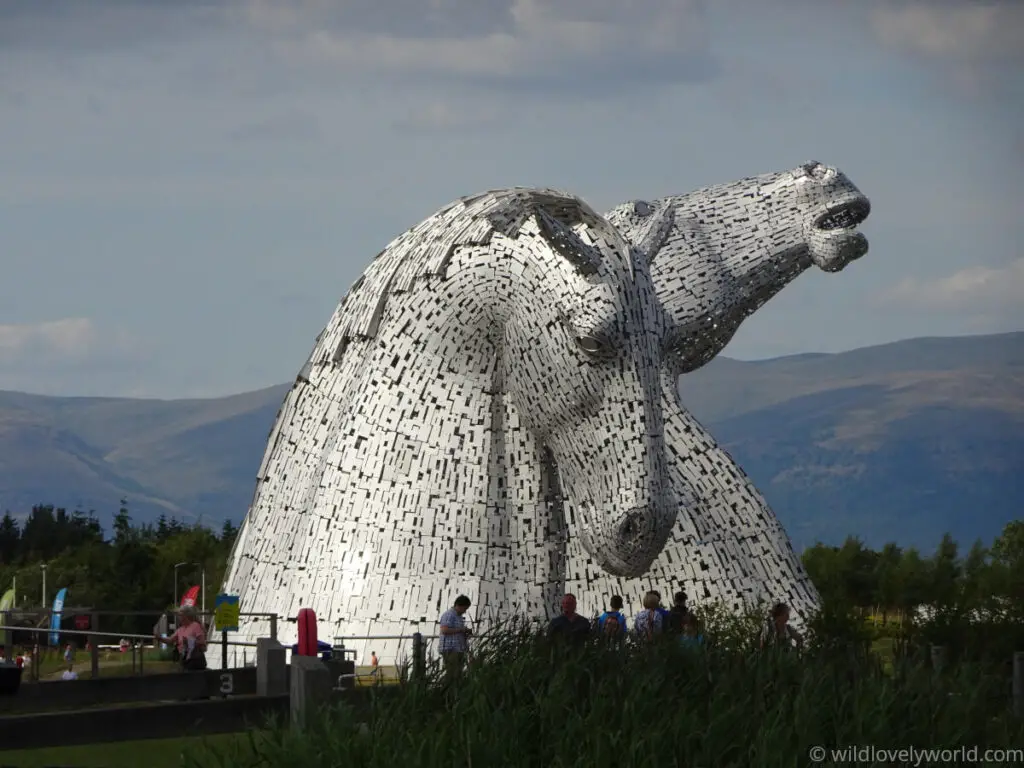 the kelpies sculptures in falkirk with mountains in the background and people observing them from below