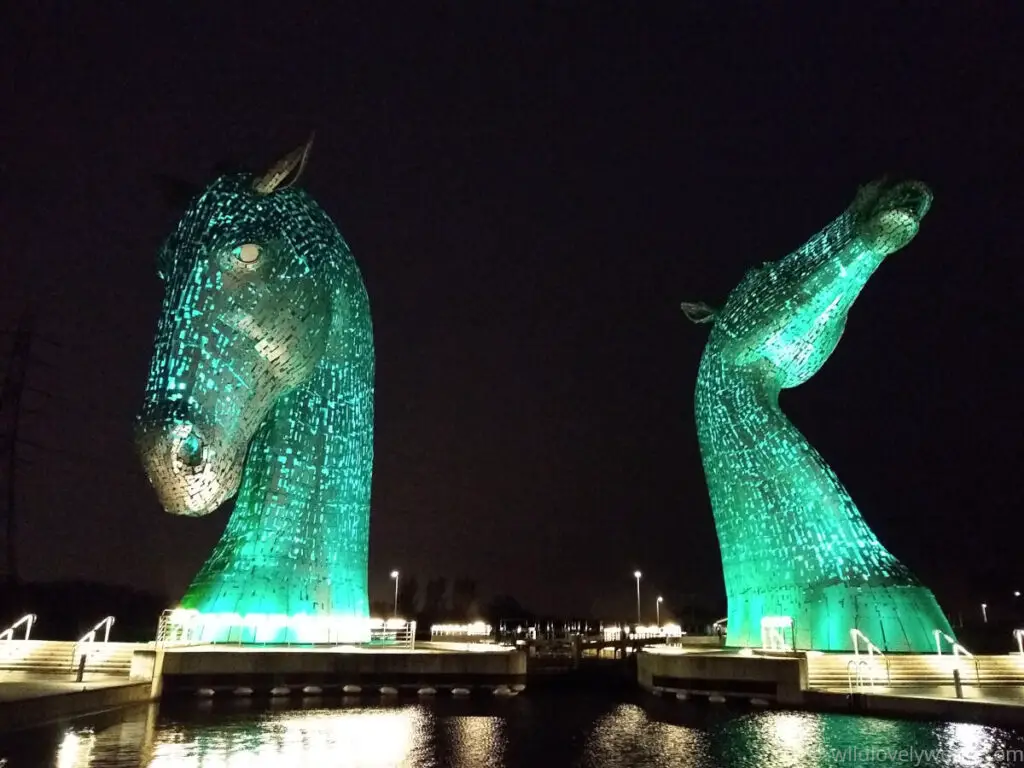 the kelpies giant horse sculptures lit up at night in the colour green with lights reflecting in the canal basin below in falkirk scotland