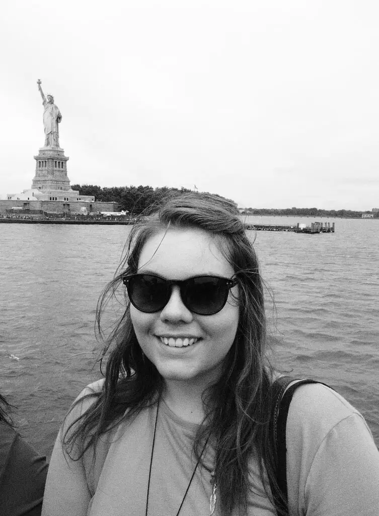 black and white photo of lauren on a boat in front of the statue of liberty, new york city
