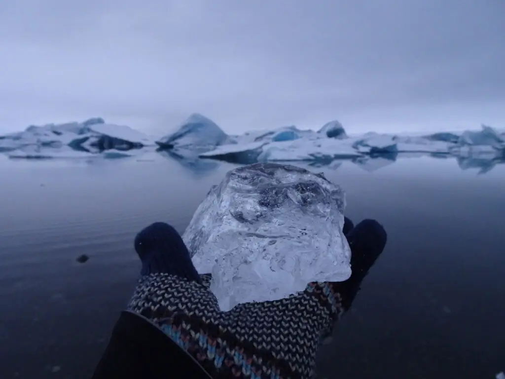 holding ice on my palm with icebergs in the background in iceland