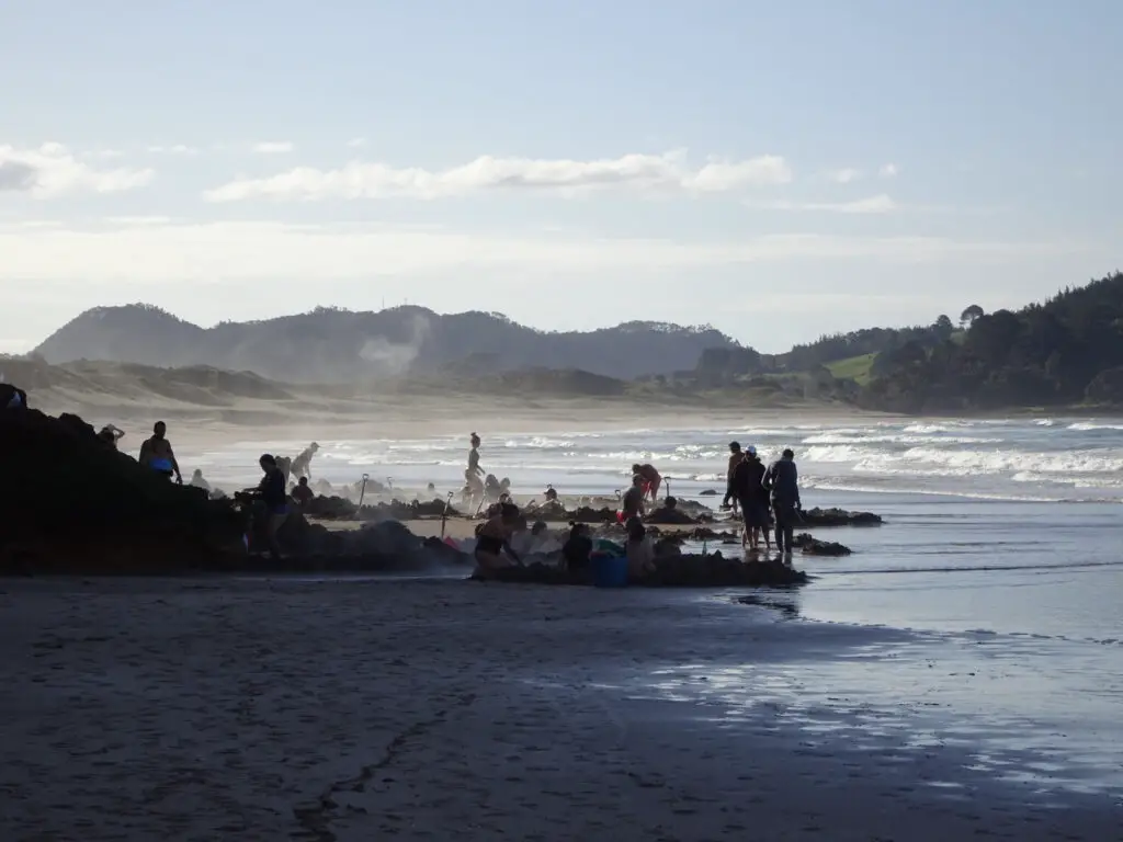 people digging hot pools in the sand at coromandel hot water beach - a must do north island experience in new zealand