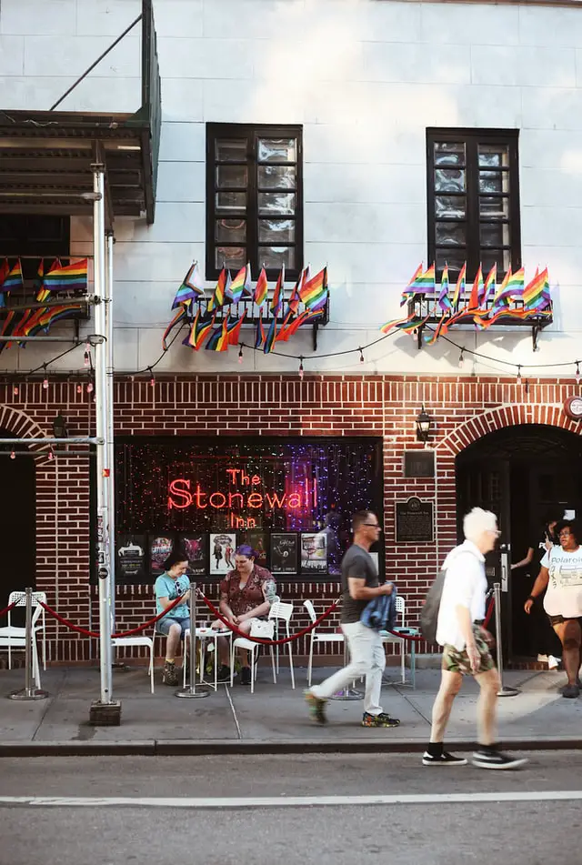 people sitting and standing outside the stonewall inn new york city with rainbow flags decorating the building