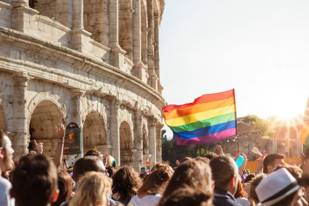 people marching with lgbtq pride flags outside the colosseum in rome italy