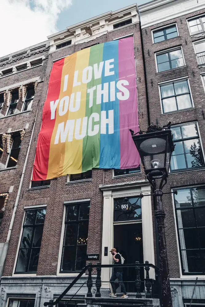 lgbtq pride rainbow flag with i love you this much written on hanging over a terrace brick building in amsterdam