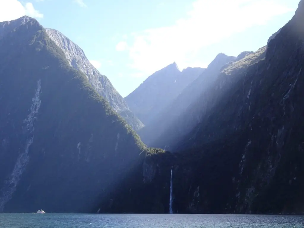 stirling falls in milford sound with a cruise boat and sunlight rays