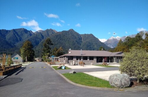 sunny day with blue sky and clearly visible green mountains at fox glacier top 10 holiday park new zealand