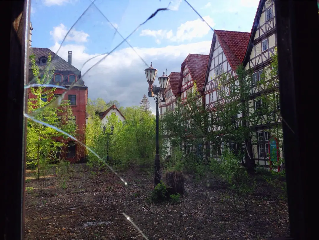 german style buildings in abandoned japanese theme park through broken window