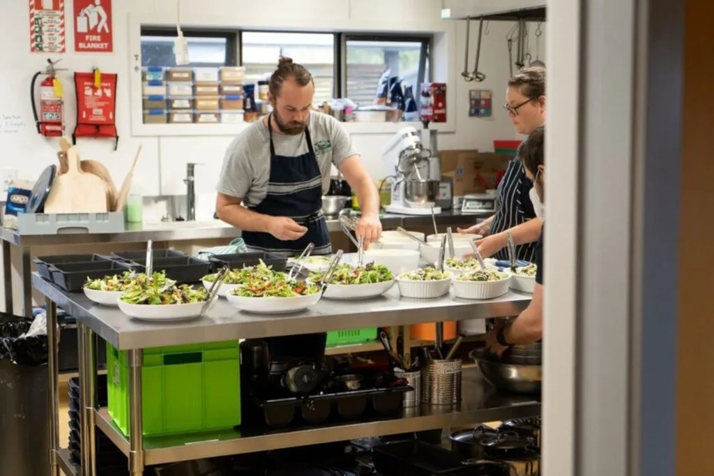 fiachra and lauren working in the kitchen preparing salads and dishes for guests at timber trail lodge