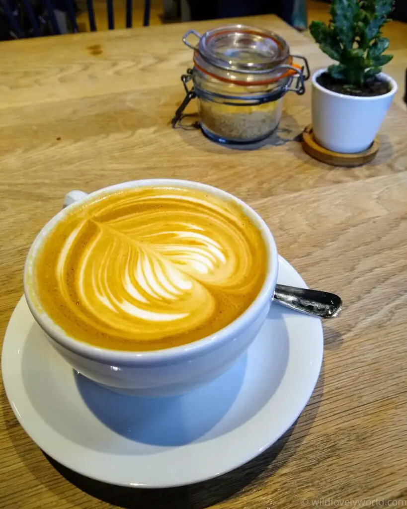 coffee in a white mug with latte art on a wooden table with a jar of sugar and a small plant in a pot - best cafes and coffee shops in edinburgh