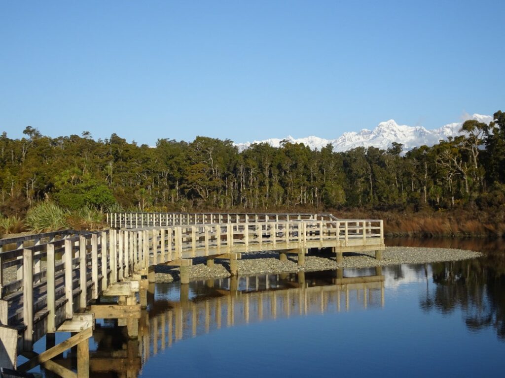 view of the bridge at gillespies lagoon on the west coast of new zealand with the snowy southern alps and rain forest in the background