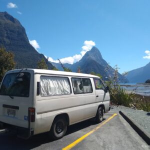 nissan caravan campervan at milford sound in new zealand with mitre peak in background on a sunny day