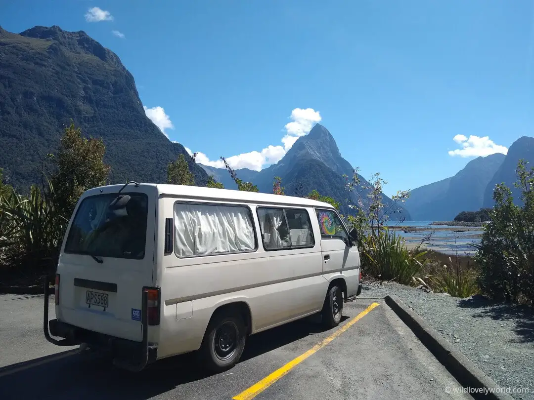 nissan caravan campervan at milford sound in new zealand with mitre peak in background on a sunny day