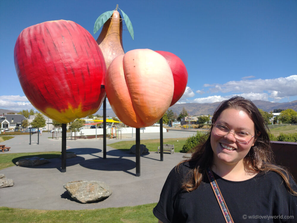 lauren smiling at the camera in front of the cromwell giant fruit sculptures - big things in the south island