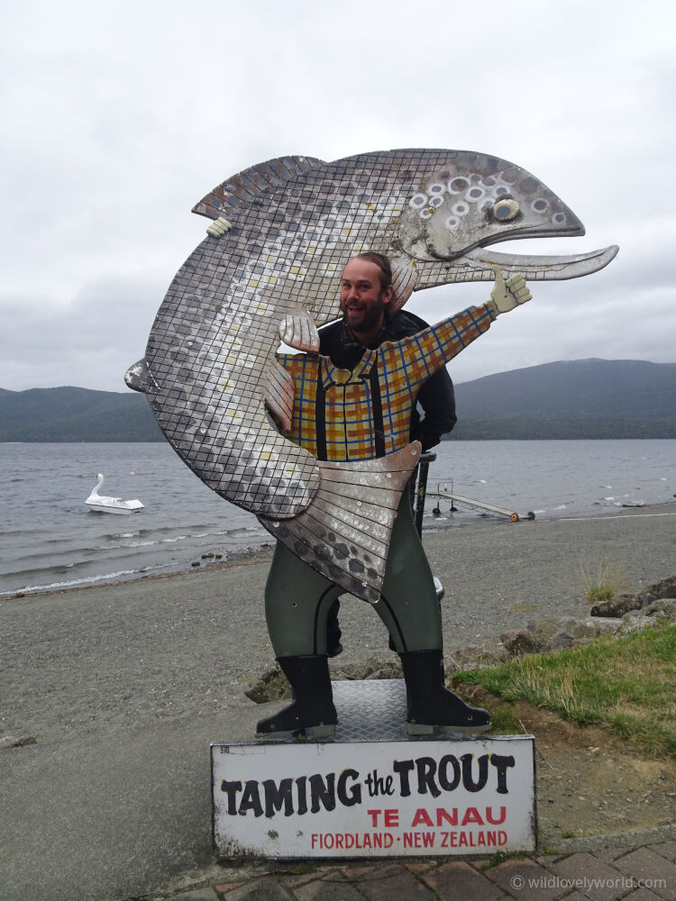 fiachra standing at the taming the trout sign by the te anau lake in fiordland new zealand