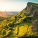 salisbury crags on the right and view of edinburgh castle and walter scott monument on the left, with golden sunlight glow coming from the left