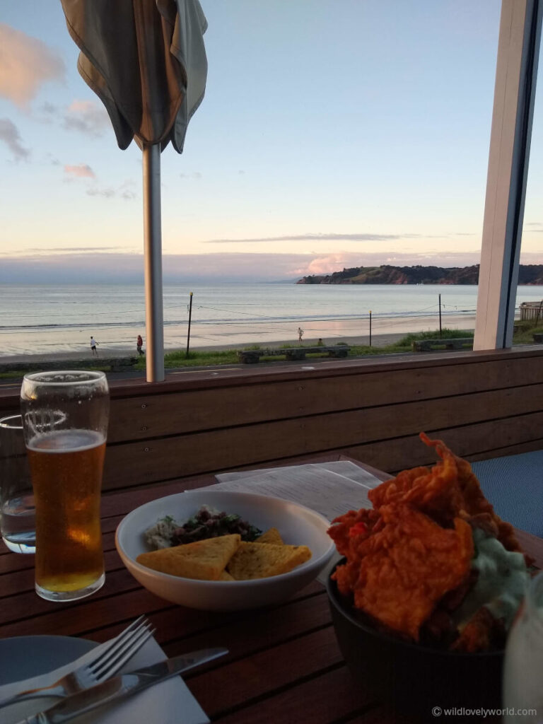 beer and snacks on a table with a view of onetangi beach at sunset - at three seven two restaurant on waiheke island