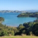 view of blue bays with a sailing boat and green rolling hills with trees - waiheke island in auckland new zealand