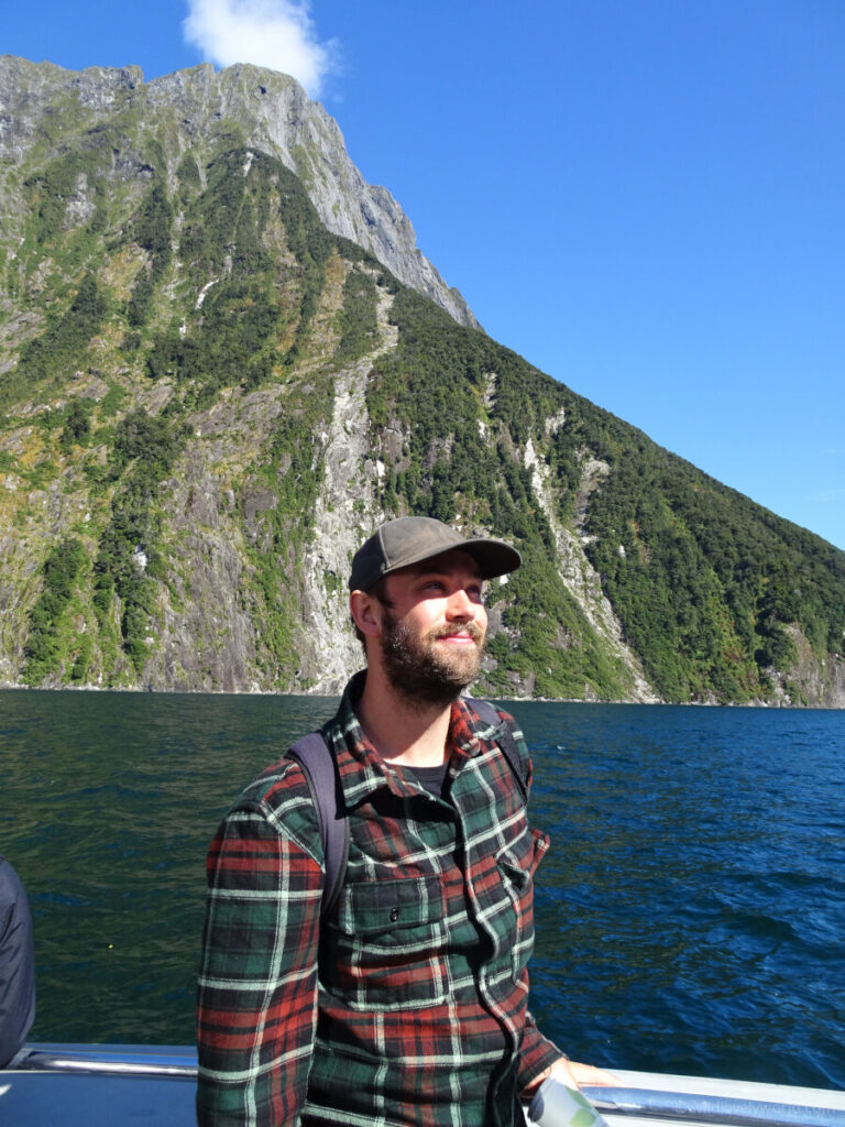 fiachra smiling viewing the scenery with fjord behind him on the milford sound cruise in new zealand