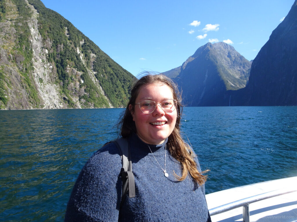 lauren smiling looking at the camera on the milford sound cruise with fjord behind her