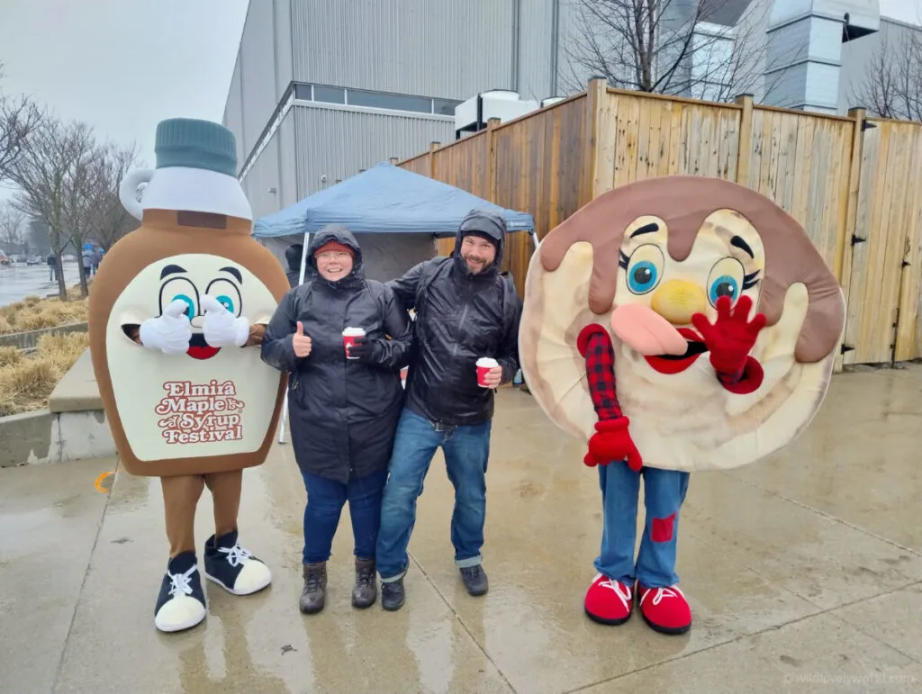 lauren and fiachra with the mascots at the elmira maple syrup festival - a maple syrup bottle and a pancake