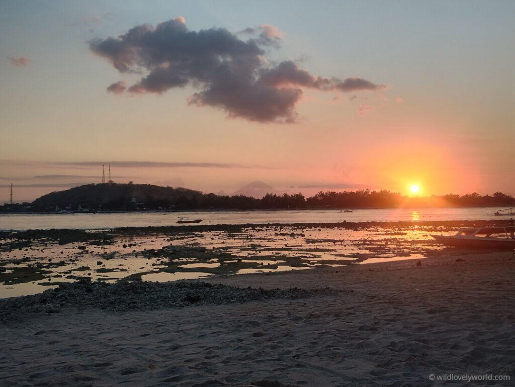 view of sunset on gili meno island at low tide. the corals are exposed at low ride. gili trawangan is visible across the water. mata air asam volcano on bali can be seen on the horizon. lombok indonesia.