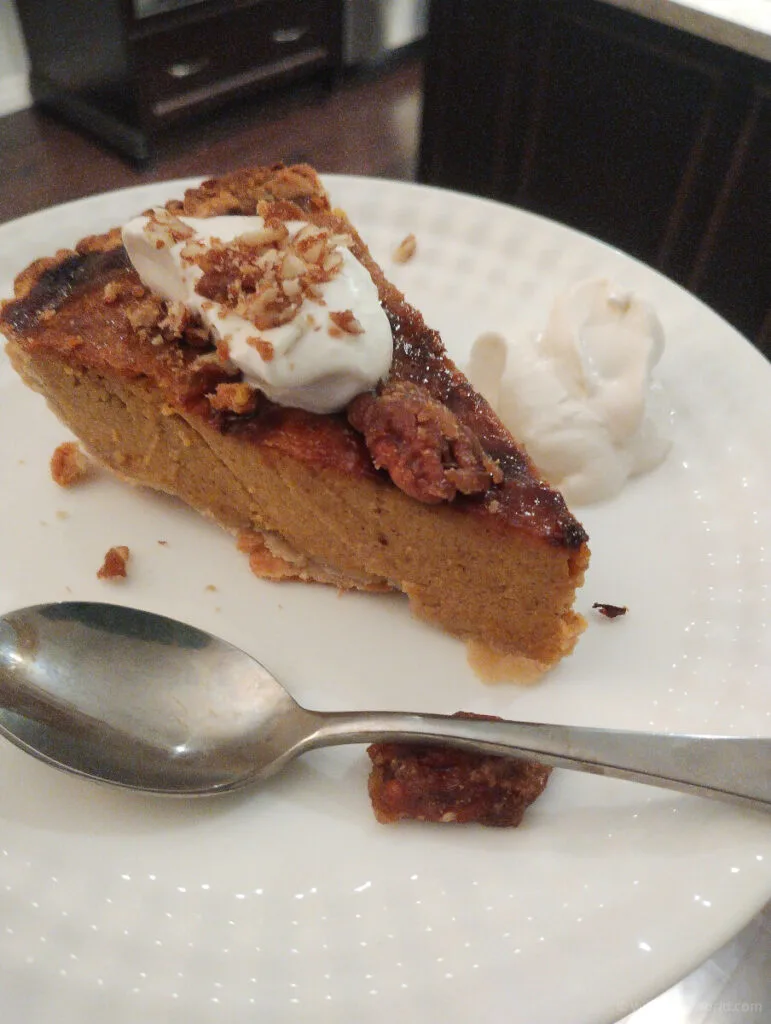 a slide of pumpkin pie topped with whipped cream on a plate with a spoon