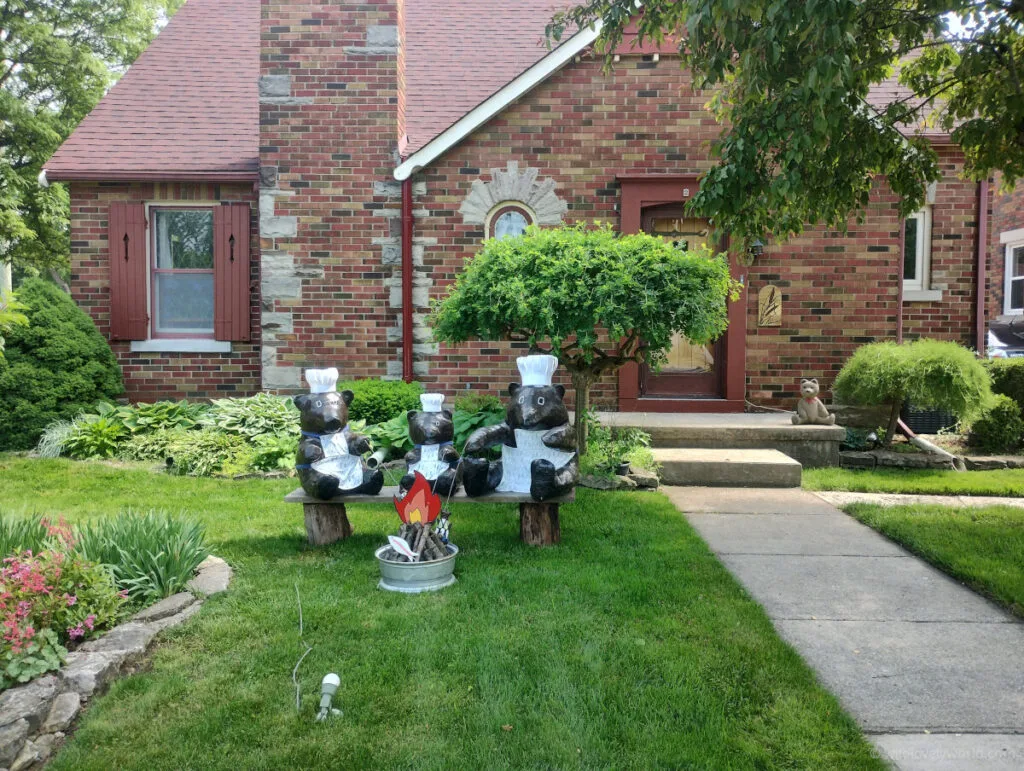 wooden bears on a front lawn toasting fish by a fire