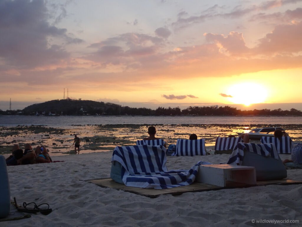 guests relaxing on the beach at sunset at le pirate gili meno resort looking toward gili t